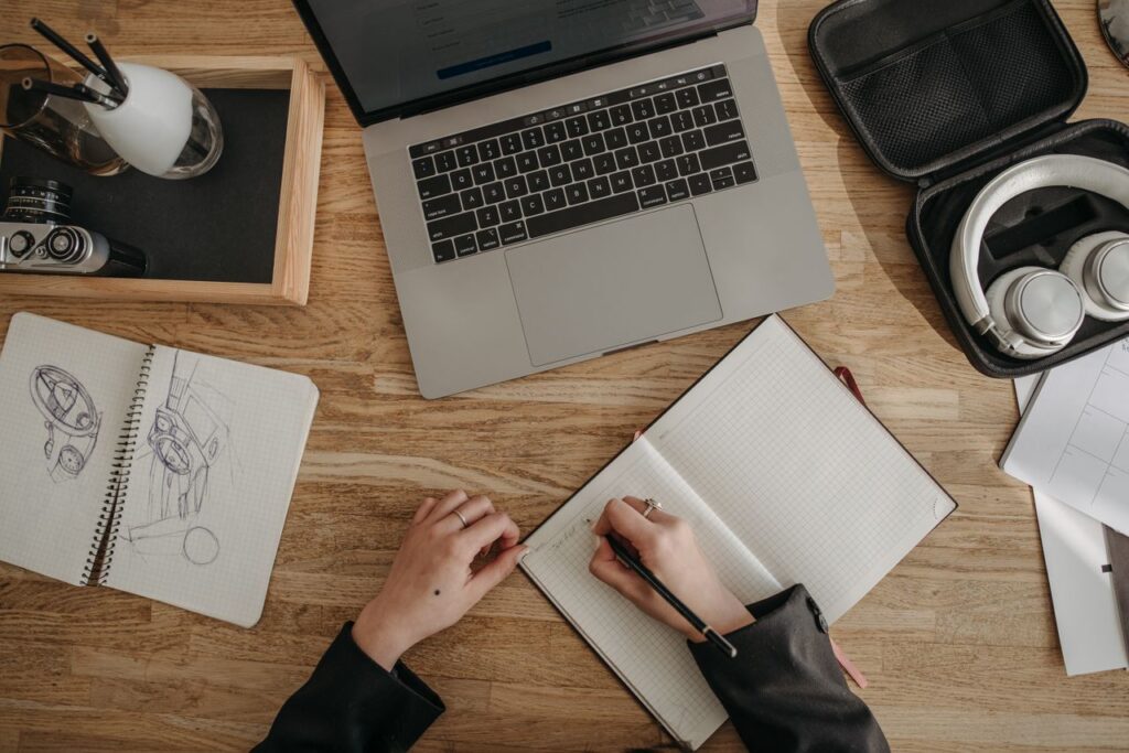 Top view of a creative workspace featuring a laptop, sketchbooks, and headphones on a wooden desk.