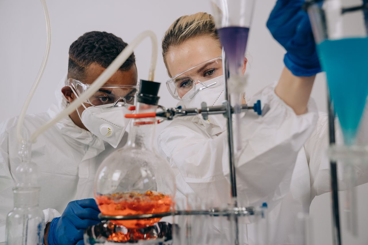 Two scientists in protective gear conducting chemistry experiments in a lab.